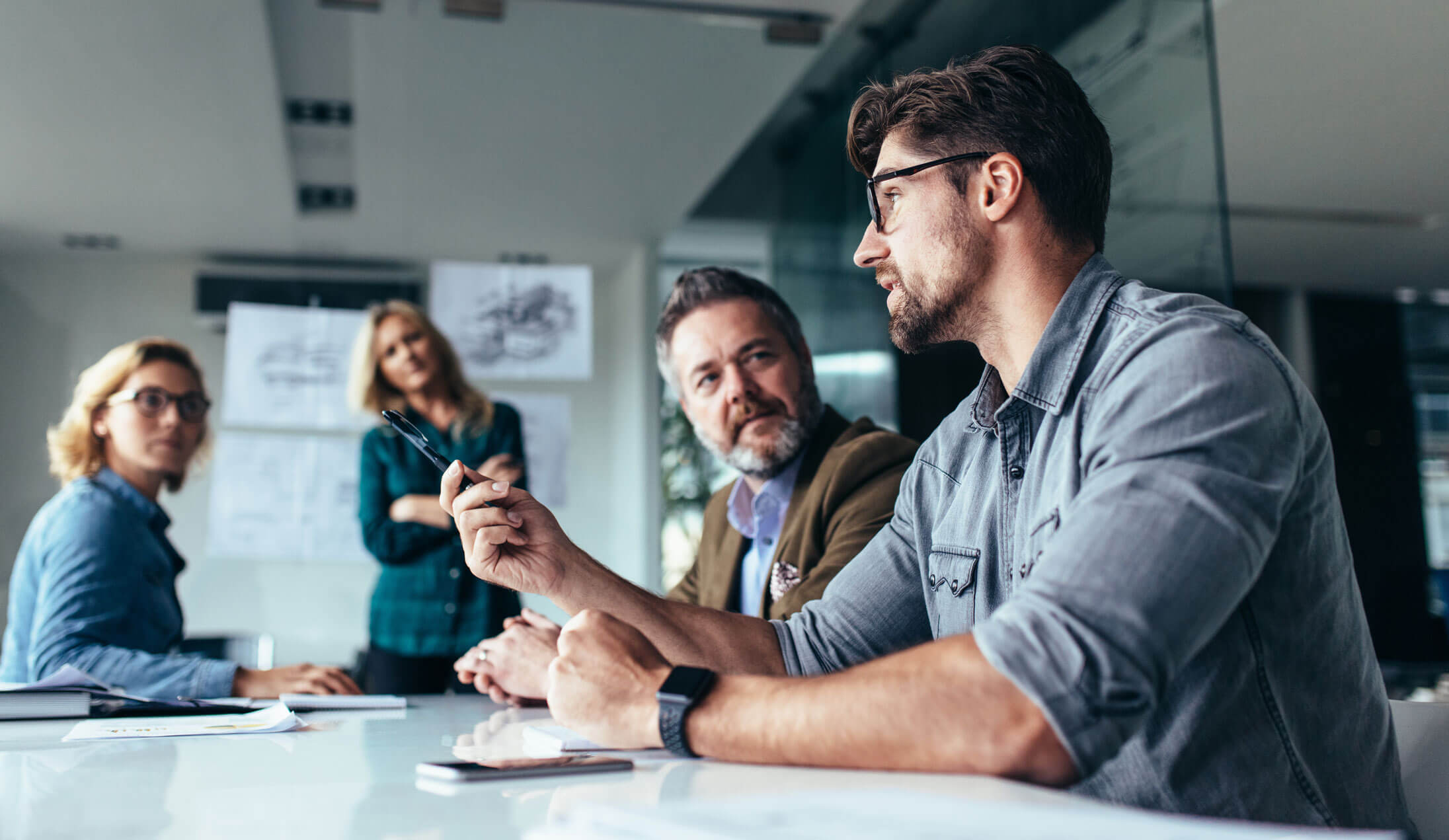 A man gesturing towards three people in a meeting.