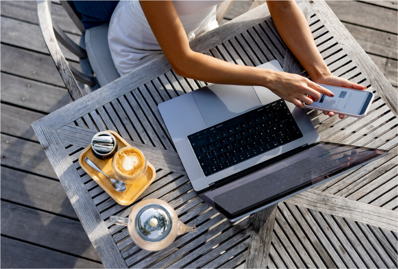 Overhead shot of a person interacting with their phone and laptop at an outdoor cafe table.