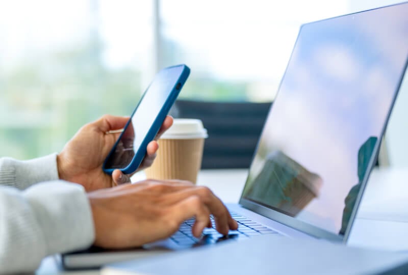 Closeup shot of a person's hands interacting with a smartphone and a laptop.