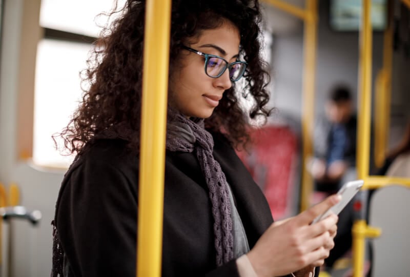Woman standing inside a bus interacting with her smartphone.