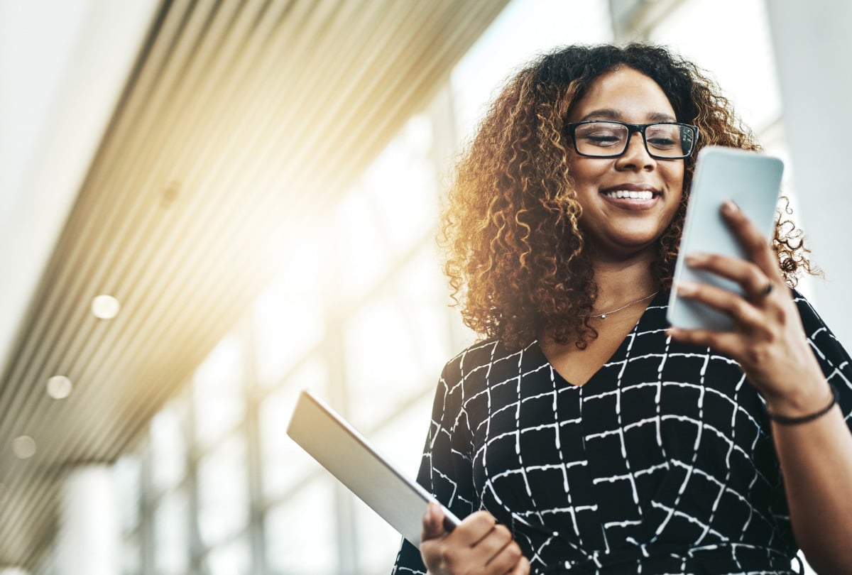 Woman smiling in a sunlit room and interacting with a smartphone.